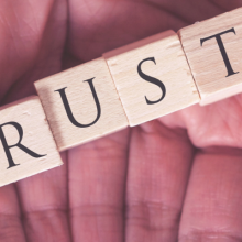 small blocks spelling TRUST, laid out in a person's two open hands