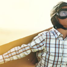 young boy pretending to fly with a pair of cardboard wings in an open field
