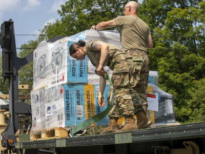 two Vermont National Guard troops unloading pallets of drinking water from a flatbed truck