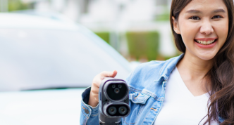 woman holding an electric vehicle charger while giving a thumbs up