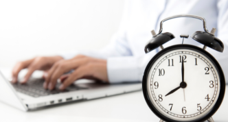 clock in foreground with hands typing on keyboard in background